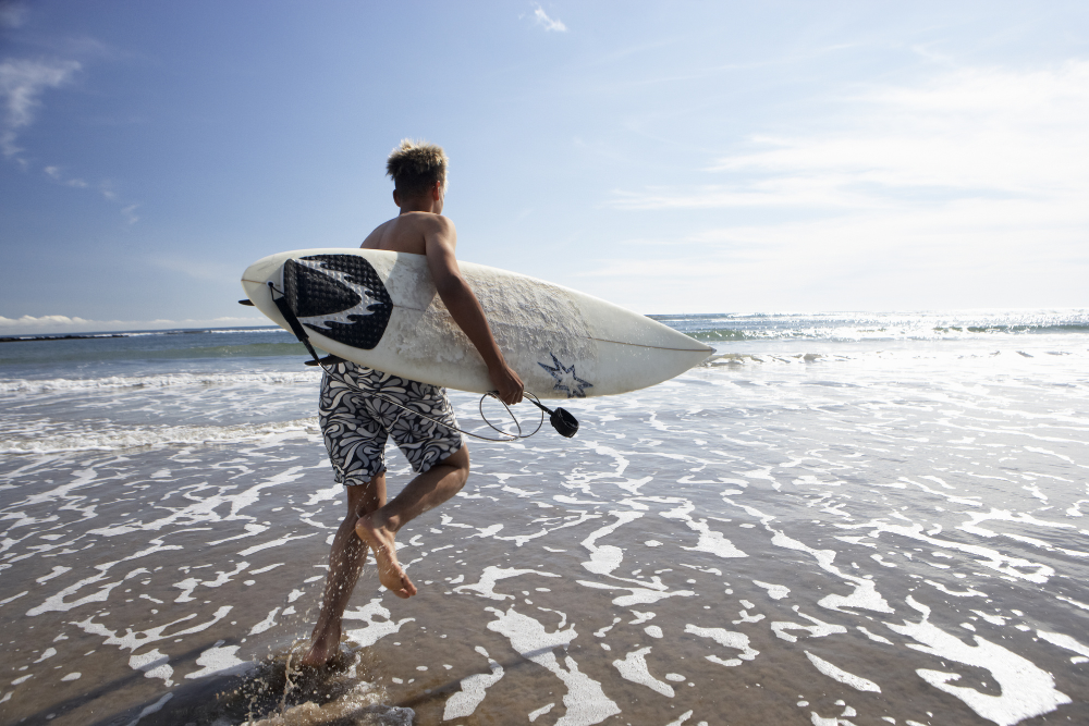 young man carrying surf board and running into ocean